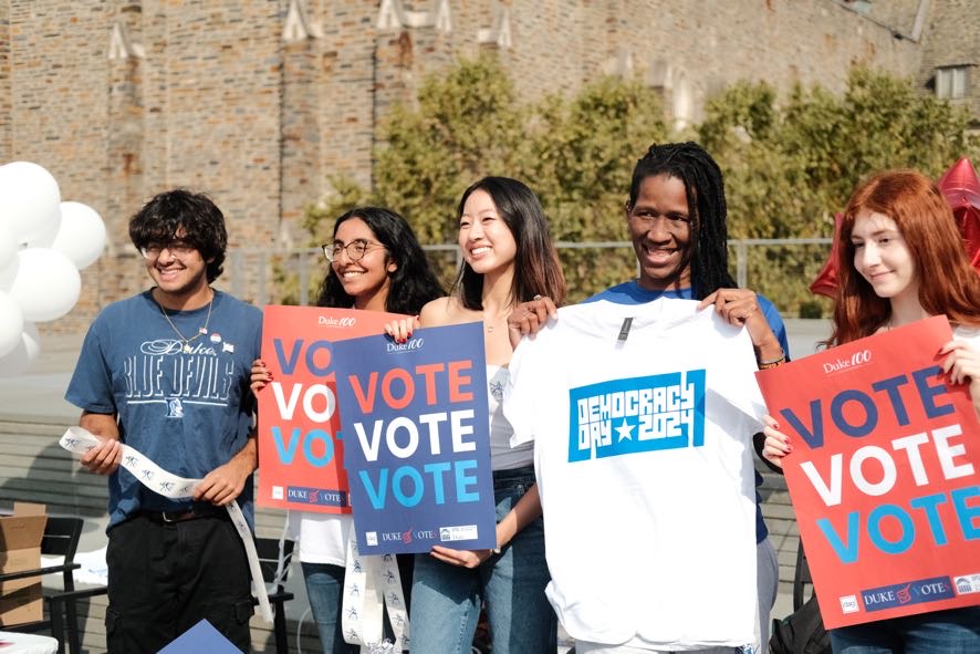 YPA members holding Vote signs and Democracy Day shirts at a campus voter education event